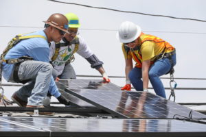 Three Southern California Edison volunteers installing solar panels on a roof.