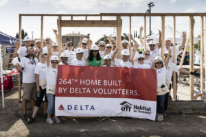 Delta volunteers with their hands in the air cheering on a construction site while holding a banner stating it is their 264th home built by Delta volunteers in partnership with Habitat.