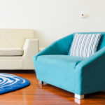 A photo of half of a couch, a blue rug, and a blue chair.