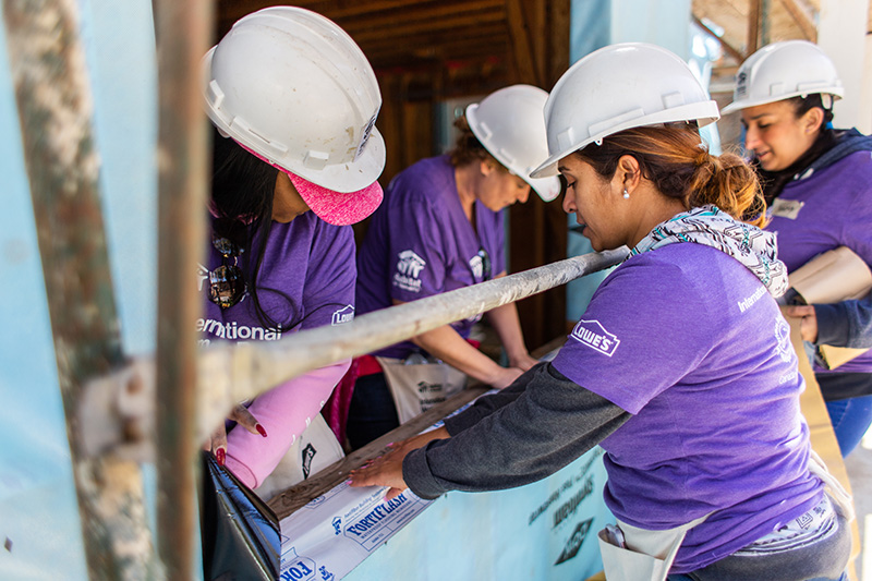 Four Lowe's Heroes volunteers installing window frames on a construction site.