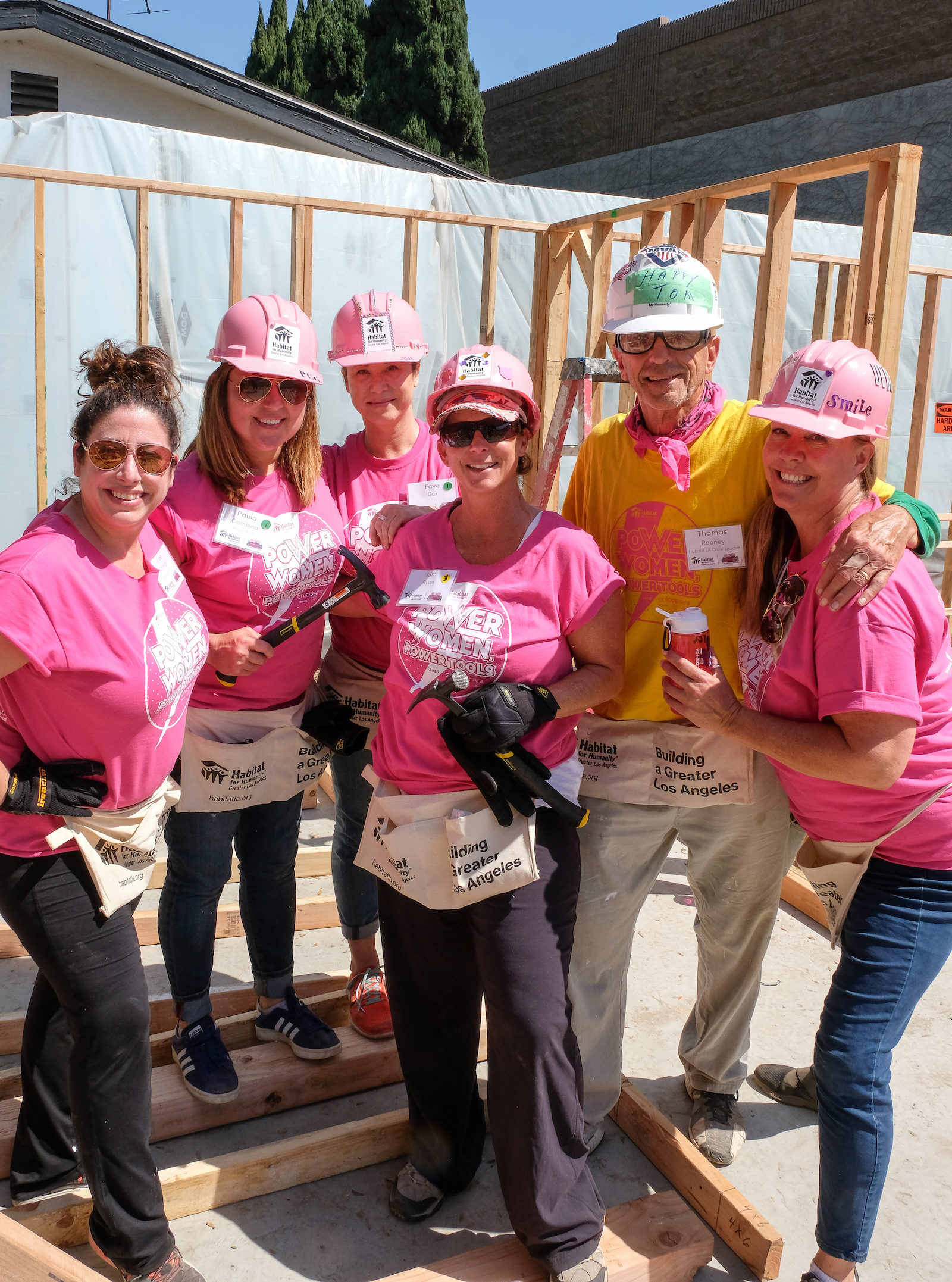 Volunteers smiling with hammers on a construction site posing for a group photo.
