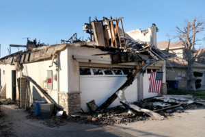 A two story home with the top story destroyed by a fire and debris around.